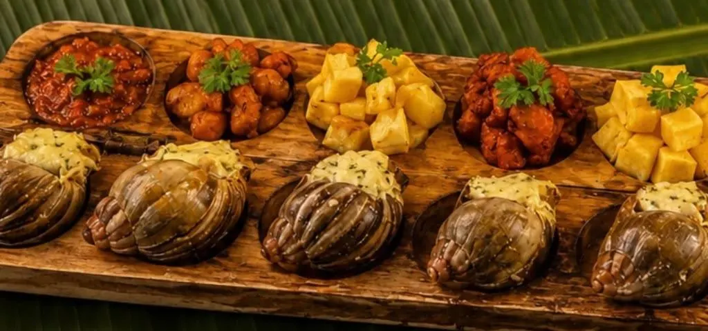 Plateau d’awalé en bois garni d’escargots gratinés, d’alloco et de bouchées en sauce