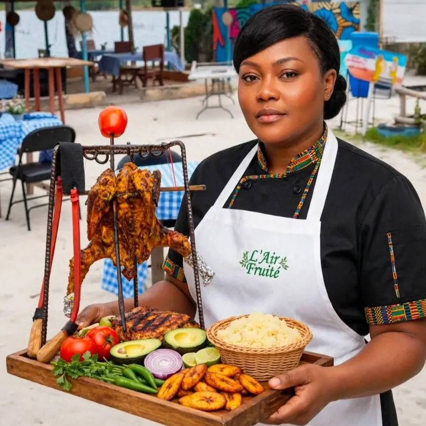 En tablier L’Air Fruité, un membre de l’équipe présente un plateau de poulet braisé, alloco, avocat et attiéké devant la paillote