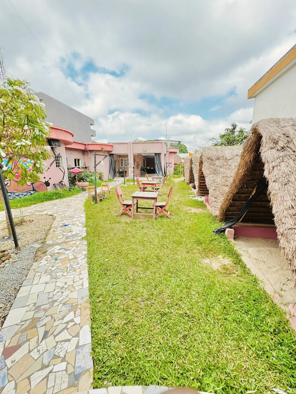 Jardin verdoyant avec tables, cases et allée pavée sous le ciel