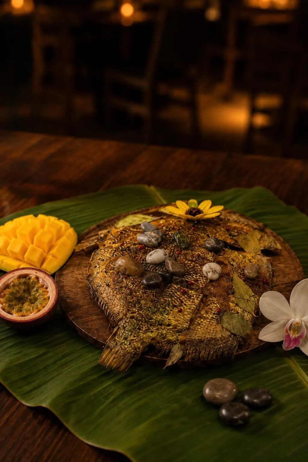 Le poisson des galets : poisson entier grillé sous des galets de rivière, sur feuille de bananier, avec mangue et fruit de la passion