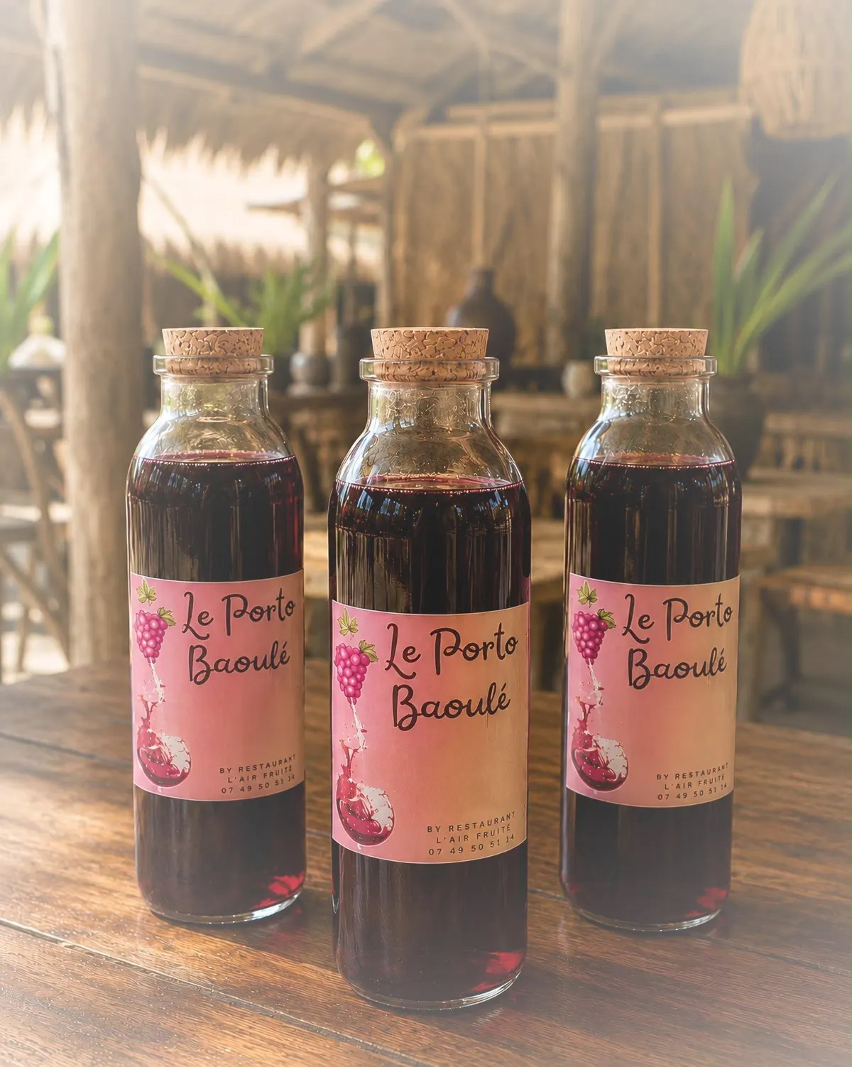 Trois bouteilles de Porto Baoulé à l’étiquette rose, sur une table en bois