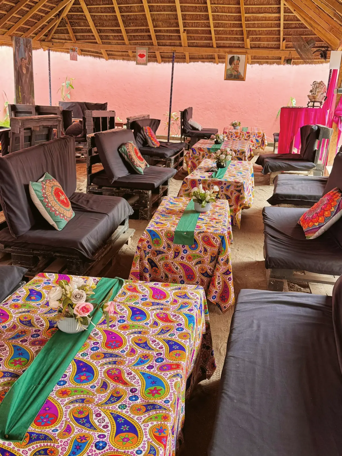 Grande paillote au toit de chaume, banquettes et nappes en wax colorées dressées pour le repas